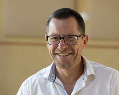 man in a white short smiling with glasses