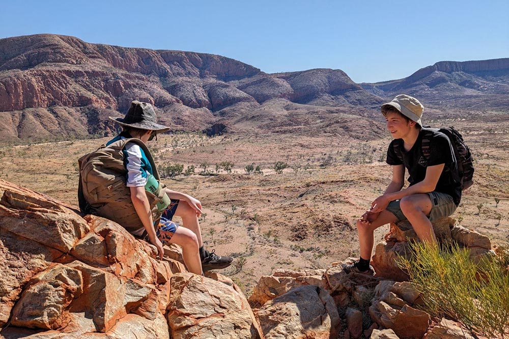 Two students on either side of the frame, sitting on rocks overlooking an outback gorge on Central Australia