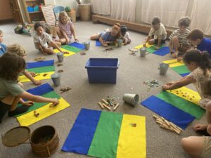 A group of young students are in a circle on the floor, with yellow, green and blue mats and counting marbles